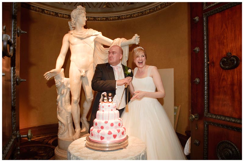 groom pulls face bride laughs about to cut cake during Woburn Sculpture Gallery wedding