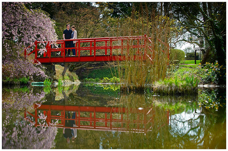 Fanhams Hall pre-wedding couple standing on red bridge over pond