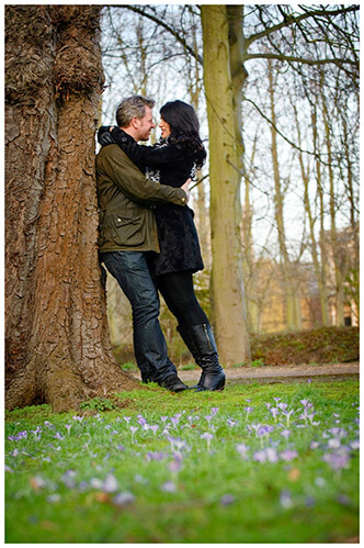 pre-wedding photography Cambridge couple embrace leaning against tree small purple flowers in foreground