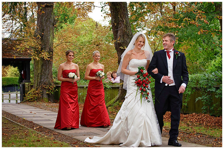 Wedding Photography at Tattersalls bride arrives on fathers arm followed by bridesmaids in red dresses
