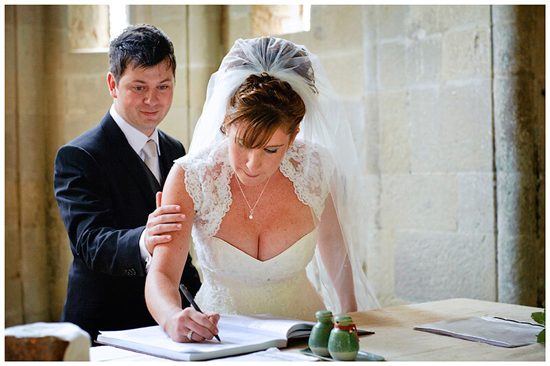 Fraternita di Romena Tuscany groom places a reasurring hand on brides arm as she signs register