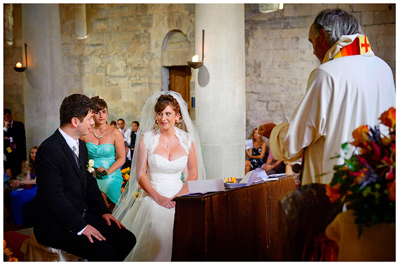 Bride groom look at each other as vicar gives sermon at Fraternita di Romena Tuscany 