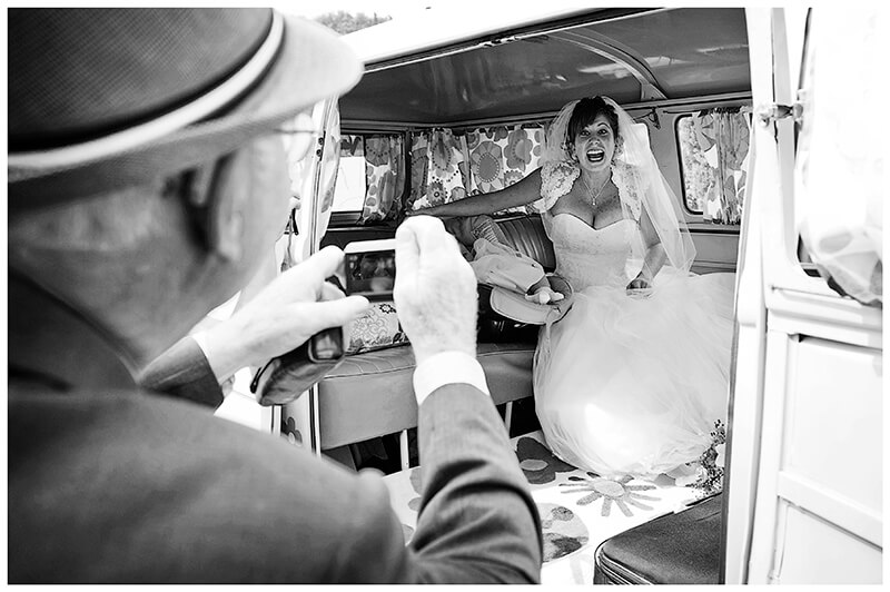 Bride smiling at old gent as he takes a photo of her in the back of the wedding car prior to leaving Fraternita di Romena Church Tuscany