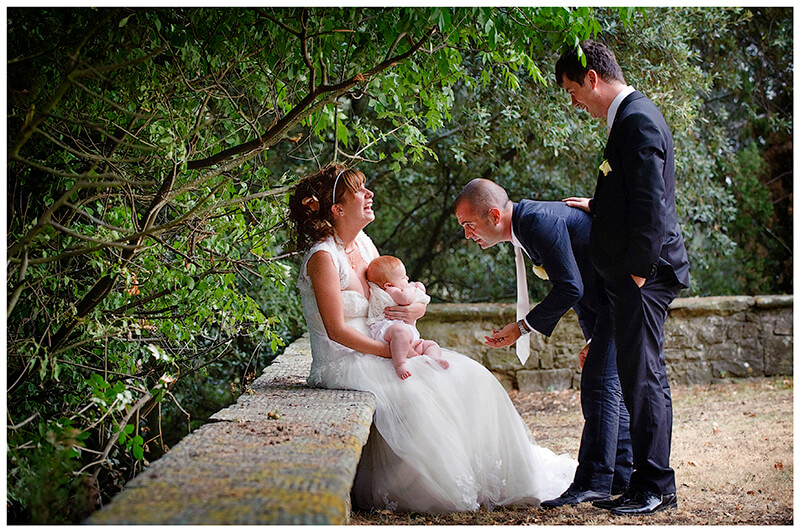 bride laughs as bestman gestures to baby being held by bride as groom looks on in gardens of Castel di Poggio Tuscany Venue