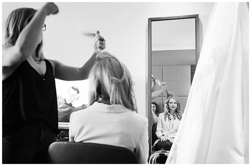 Bride having hair done reflected in mirror mans face on TV Cambridge Wedding Photography