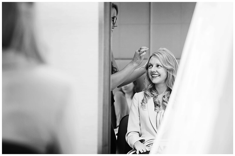 Smiling bride reflected in mirror as she has hair done Cambridge Wedding Photography