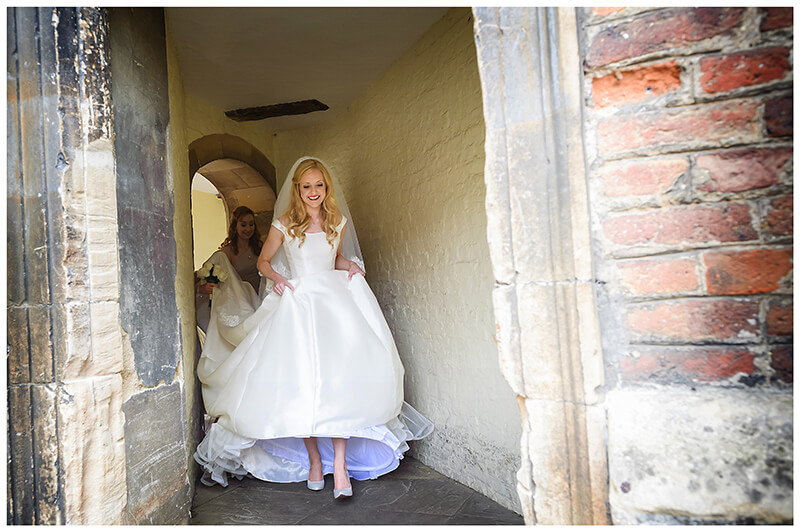 Bride walking through passageway lifting front of dress 