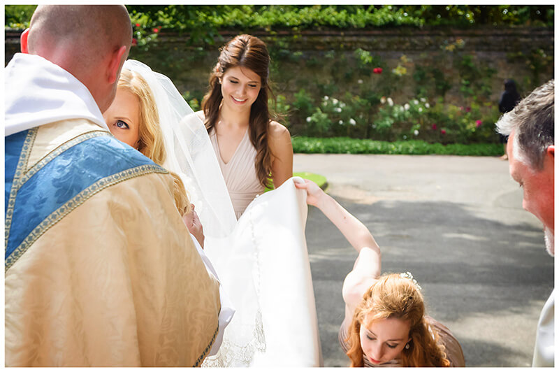 bride talking to vicar as bridesmaids adjust dress train