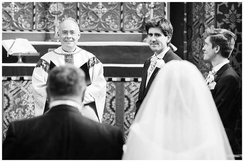 Groom looking at bride as she walks down aisle Queens College chapel