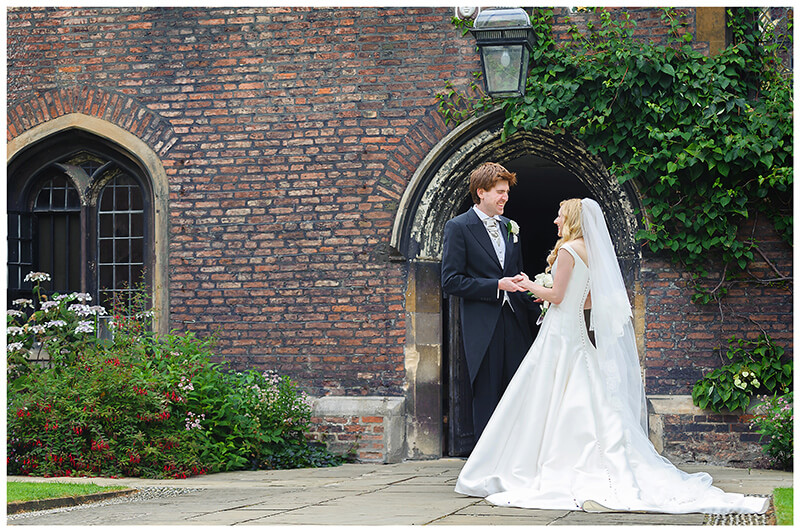 Bride groom standing in quad of Queens College Cambridge laughing and holding hands