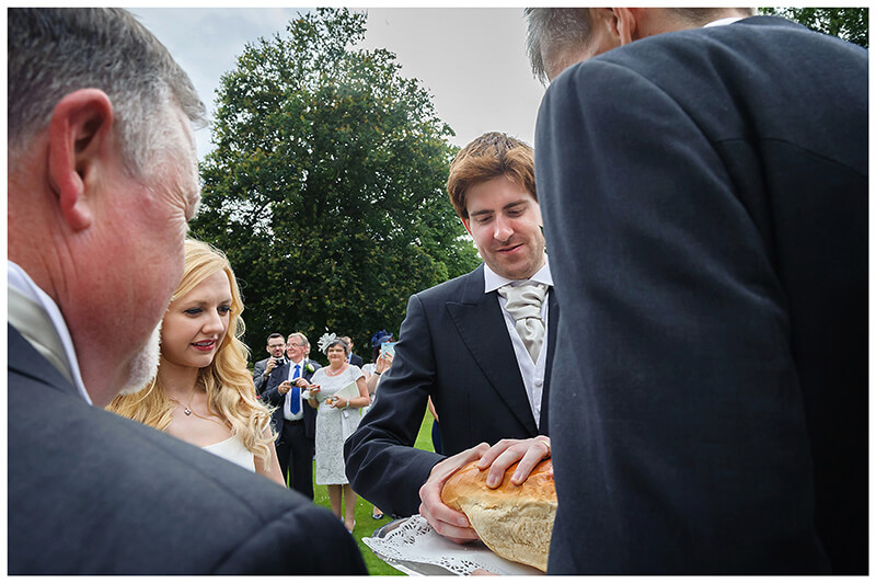 Groom takes some bread during bread and salt ceremony in front of Newnham College Cambridge 