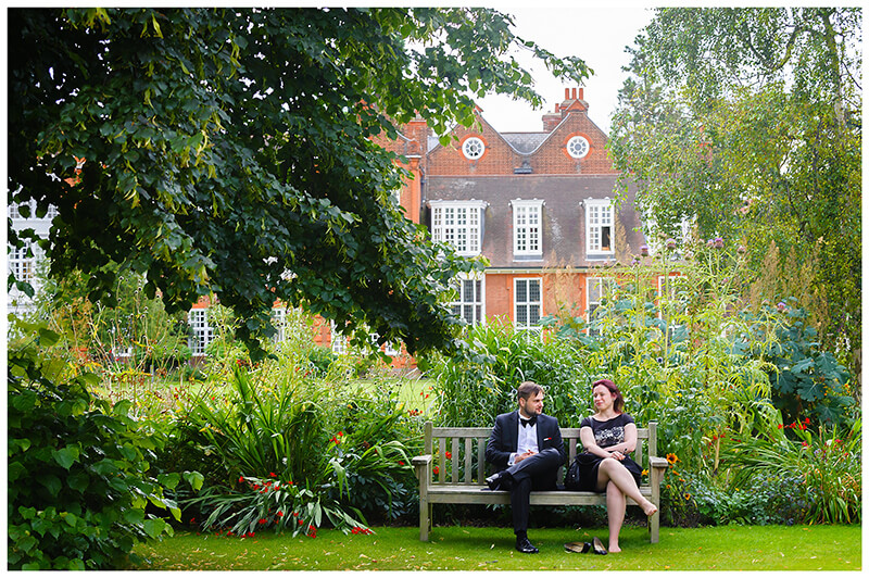 couple of wedding guests sitting on a bench in the grounds of Newnham College Cambridge