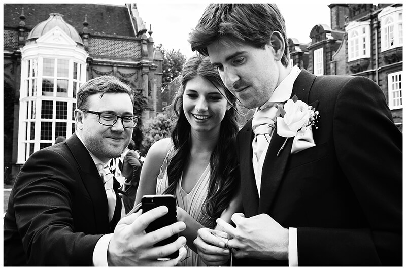 Groom and guests looking at photos on the back of phone 