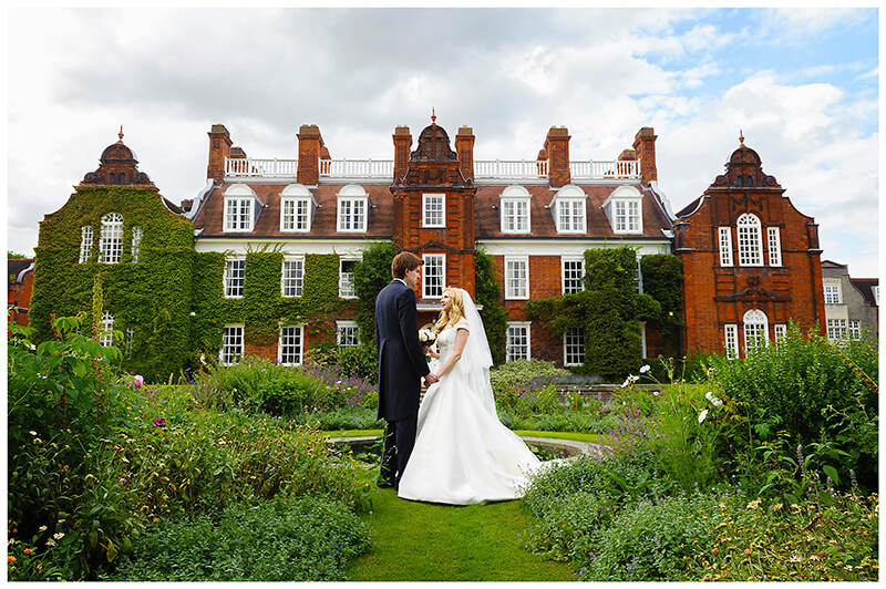 Bride and groom hold hands in gardens of Newnham College Cambridge