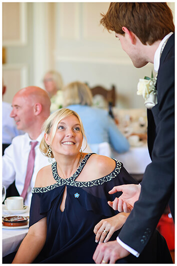 seated female wedding guest talking to standing groom