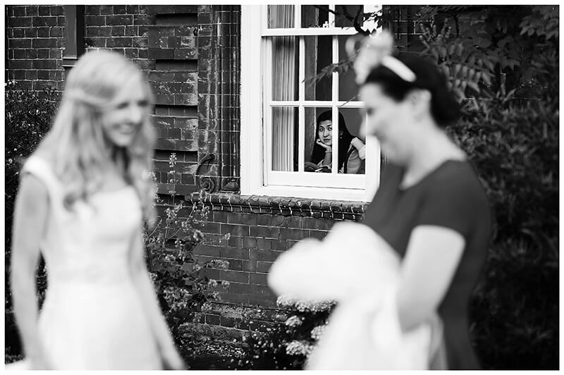 lady watches bride dreamily from window at Newnham College Cambridge