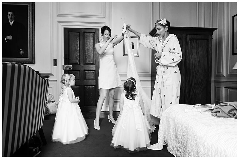 bride and bridesmaid lift wedding dress watched by two flower girls during brides Trinity College wedding preperations