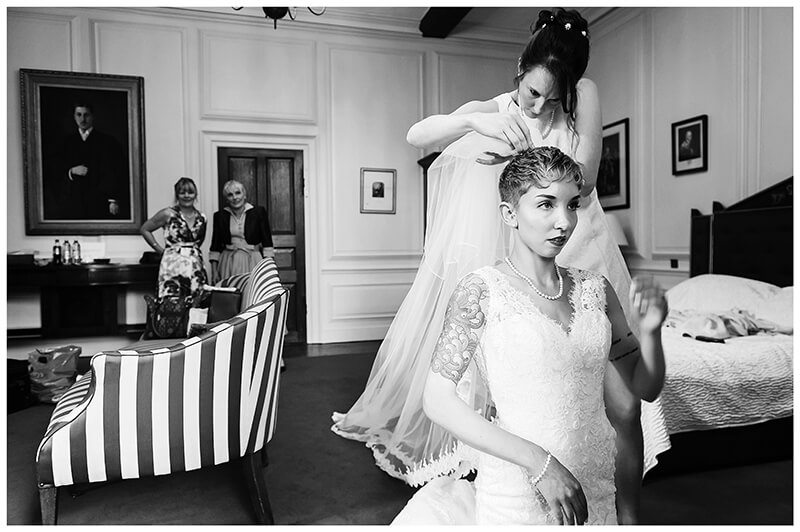 bridesmaid fitting veil to brides head mother in back ground
