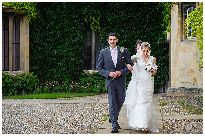 smiling bride on arm of brother as they walk to trinity Colleg chapel