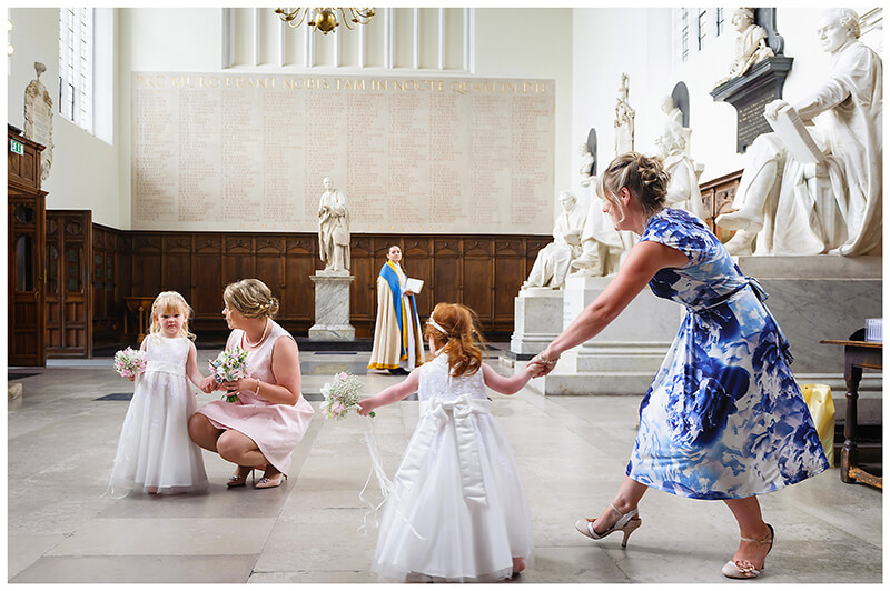 flower girls and their mothers in main entrance to Trinity College chapel vicar in background