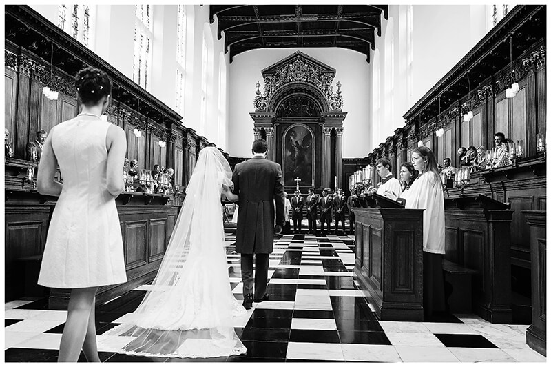 bridal party walking down aisle towards groom and his ushers at alter of Trinity College Chapel