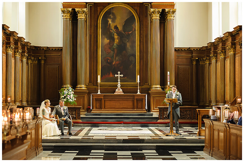 Wedding guest reading during Trinity College chapel wedding bride groom sitting