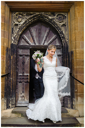 bride in front of large wooden door holding bouquet and veil at Trinity College wedding