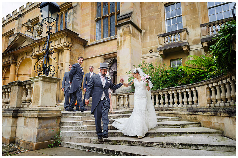 groom helps bride walk down stone steps at Trinity College at Trinity College wedding