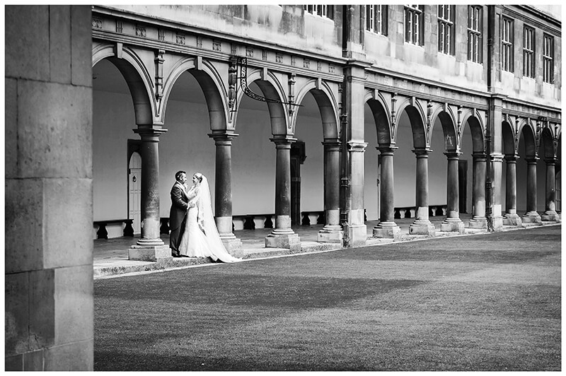 bride and groom standing in the middle of arched pillars at Trinity College wedding