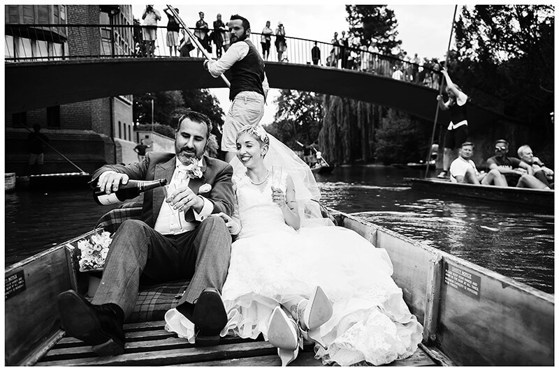 bride & groom pour champagne riding on a punt on river Cam