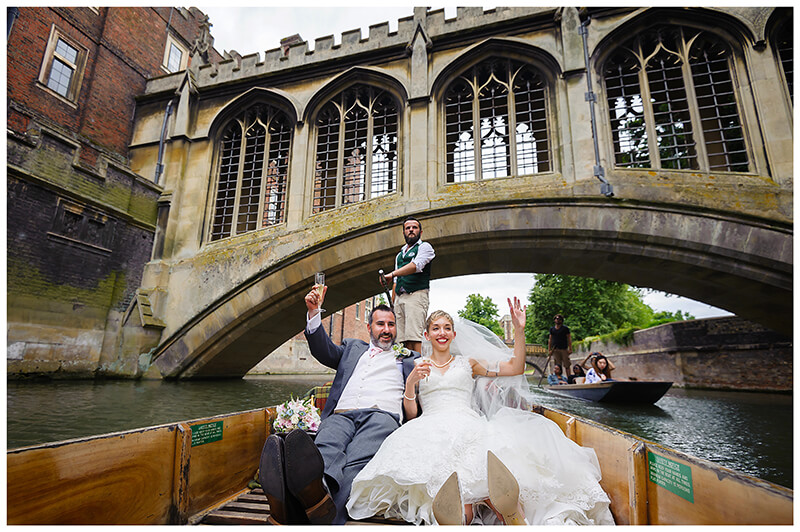 bride and groom waving as they go punting on river cam under bridge of sighs