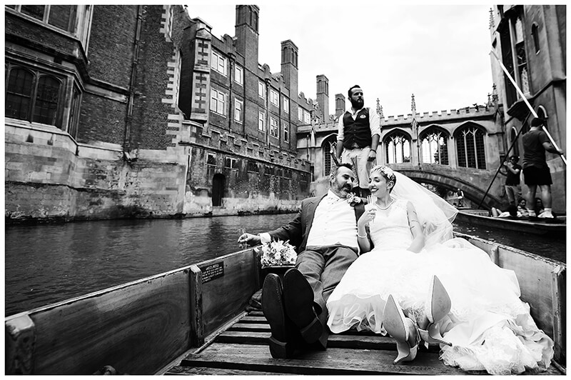 bride and groom sitting on river punt passing St Johns College in Cambridge