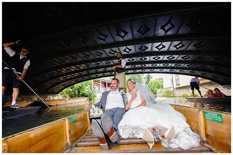 bride and groom passing under bridge riding in punt on river in Cambridge