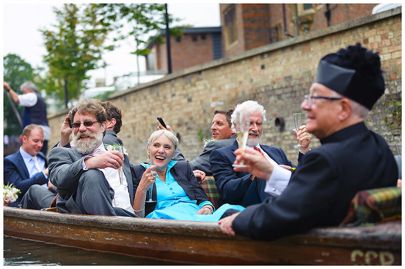 smiling wedding guests raise glasses whilst riding on punt