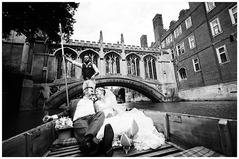 Wedding couple in punt on river in Cambridge kiss with bridge of sighs behind them