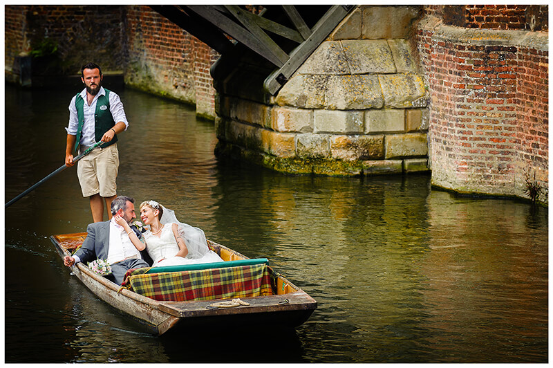 bride caresses grooms face whilst sitting in punt on river cam
