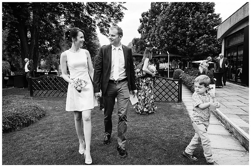 Wedding couple walking hand in hand watched by young boy