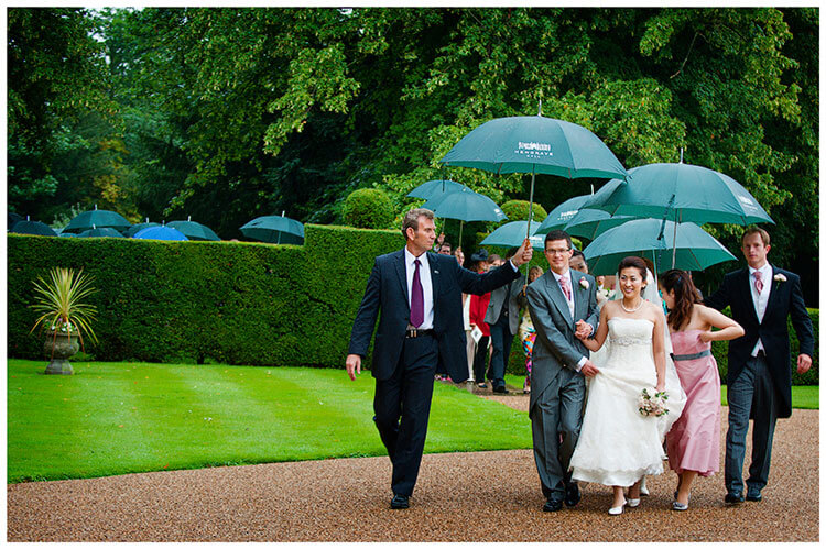 hengrave hall wedding party walking under umbrellas