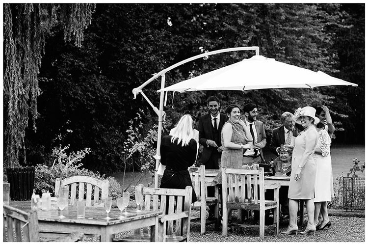 wedding guests take cover from rain under a large parasol
