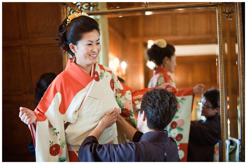 Japanese bride being dressed in orange kimono
