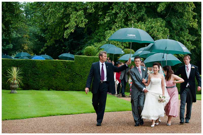 bridal party walking in rain under umbrellas to reception