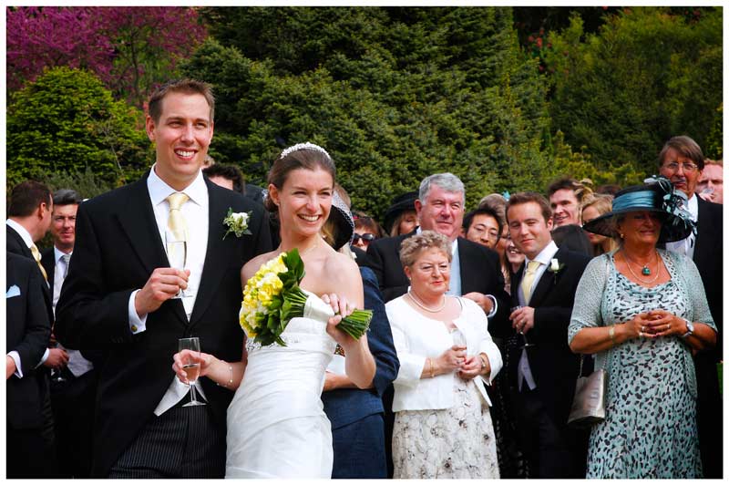 happy bride standing next to groom guests behind in beautiful gardens of Jermyn's House