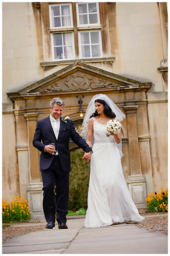 Christ’s College wedding smiling bride groom hold hands as they walk along path