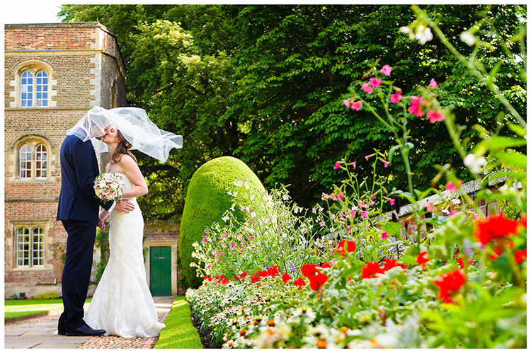 Choosing your perfect wedding photographer bride groom kiss in cambridge college gardens whilst veil blows over them