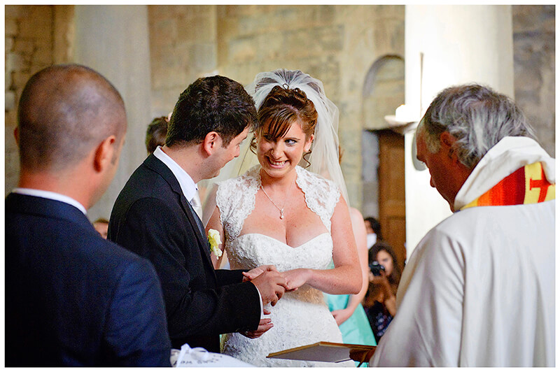 Bride groom look at each other as groom places ring on brides finger Fraternita di Romena Church Tuscany 