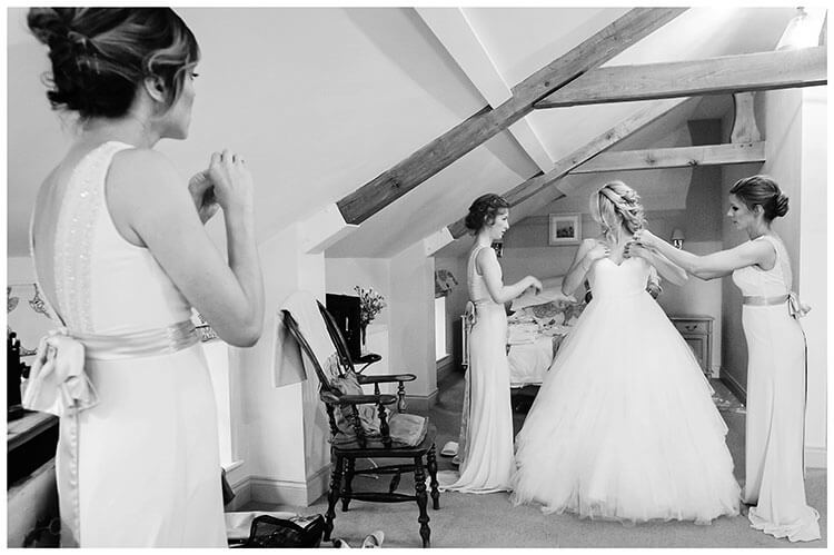 Bride assisted by bridesmaids getting into wedding dress at Cambridgeshire village wedding