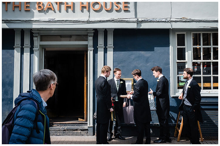 Groom and ushers outside pub The Bath House in Cambridge sorting last minute items before heading to Kings College for Ceremony passer by looks at them