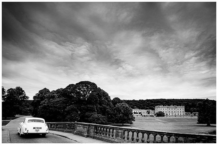 White Wedding car drives over bridge with chatsworth House in Background