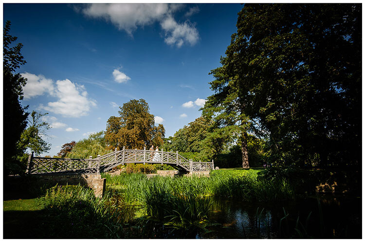 Bride and groom enjoy a moment together on ornate wooden bridge in the grounds of Cambridgeshire wedding venue Island Hall, Godmanchester favourite wedding photography 2018