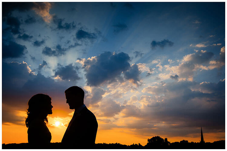 silhouette of wedding couple against a deep bllue and orange sky with church spire in background favourite wedding photography 2018